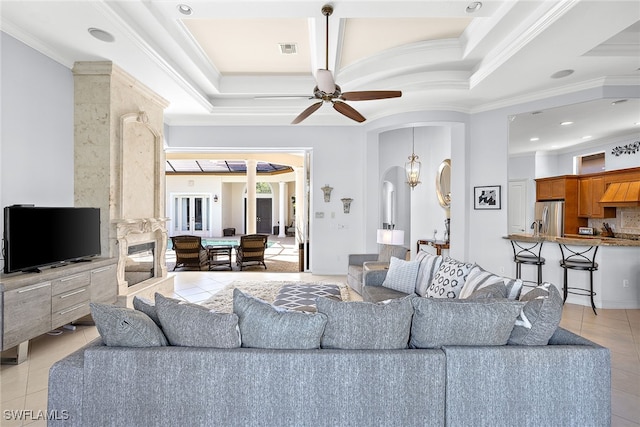 tiled living room with a tray ceiling, ornamental molding, and ceiling fan with notable chandelier