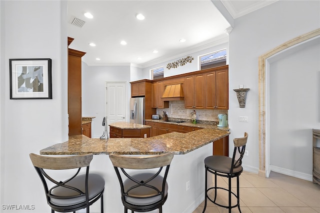 kitchen featuring a breakfast bar, kitchen peninsula, dark stone countertops, stainless steel fridge with ice dispenser, and decorative backsplash