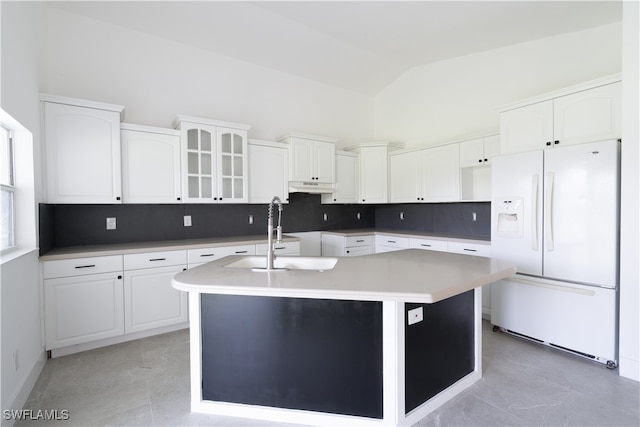 kitchen with white cabinetry, sink, white refrigerator with ice dispenser, a kitchen island with sink, and vaulted ceiling