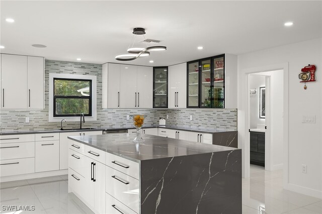 kitchen with dark stone counters, a spacious island, sink, decorative backsplash, and white cabinetry