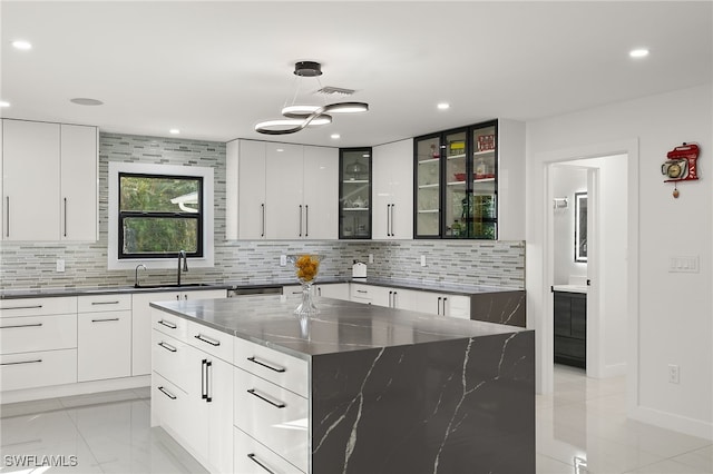 kitchen with sink, tasteful backsplash, white cabinetry, dark stone countertops, and a large island