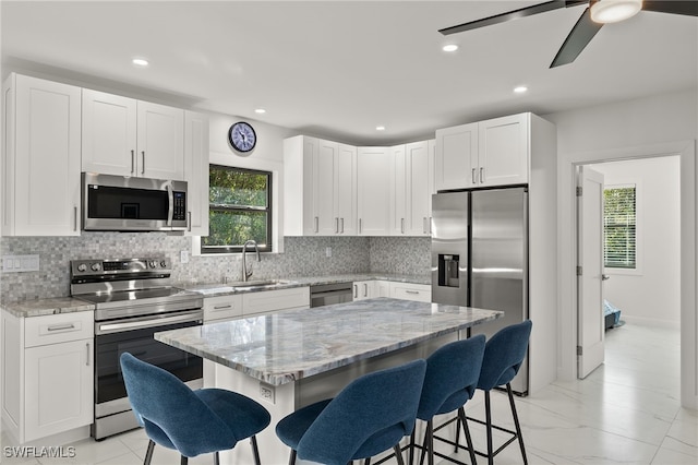 kitchen with appliances with stainless steel finishes, white cabinetry, a kitchen bar, a center island, and light stone countertops