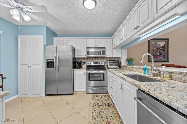 kitchen featuring light stone countertops, sink, light tile patterned floors, white cabinets, and appliances with stainless steel finishes