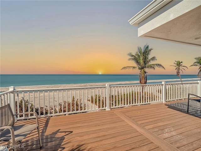 deck at dusk featuring a beach view and a water view