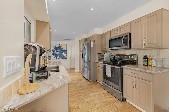 kitchen with light brown cabinets, stainless steel appliances, light stone counters, light hardwood / wood-style flooring, and backsplash