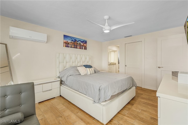 bedroom with ceiling fan, light hardwood / wood-style floors, an AC wall unit, and connected bathroom