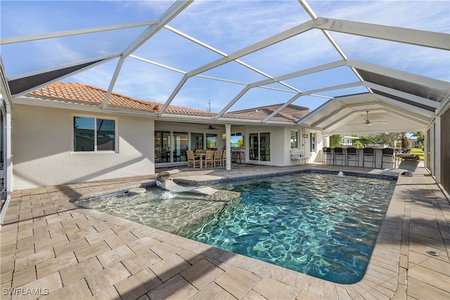 view of swimming pool with glass enclosure, ceiling fan, pool water feature, a patio area, and a bar