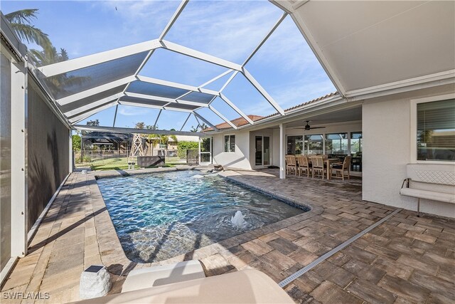 view of swimming pool featuring pool water feature, ceiling fan, a lanai, a bar, and a patio