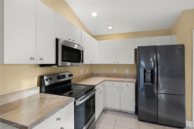 kitchen with white cabinetry, stainless steel appliances, light tile patterned floors, and vaulted ceiling