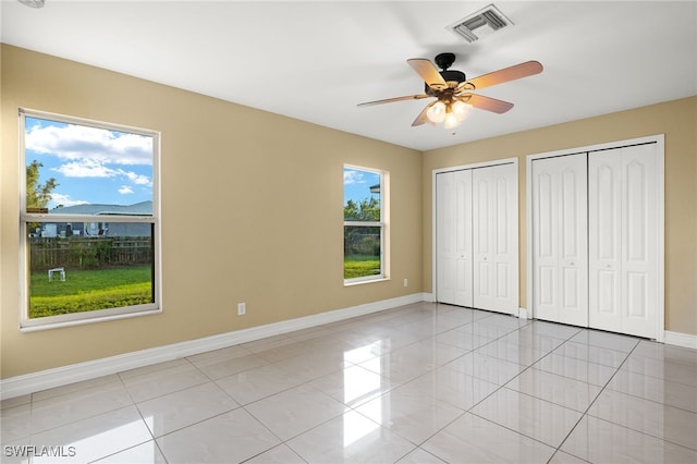 unfurnished bedroom with multiple closets, ceiling fan, and light tile patterned flooring