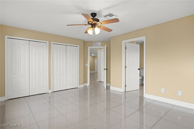 unfurnished bedroom with connected bathroom, two closets, ceiling fan, and light tile patterned flooring