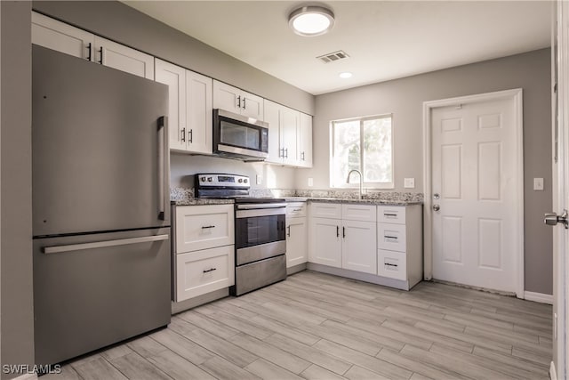 kitchen with white cabinets, light wood-type flooring, stainless steel appliances, and light stone counters