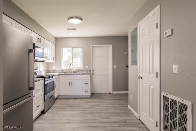 kitchen featuring appliances with stainless steel finishes, light stone counters, sink, light hardwood / wood-style flooring, and white cabinetry