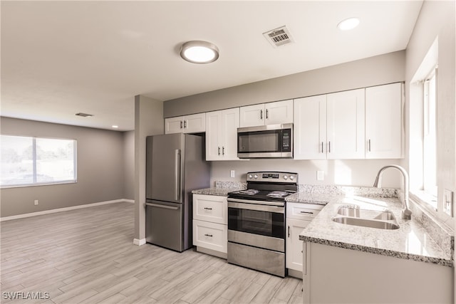 kitchen featuring appliances with stainless steel finishes, light stone counters, sink, light hardwood / wood-style flooring, and white cabinetry