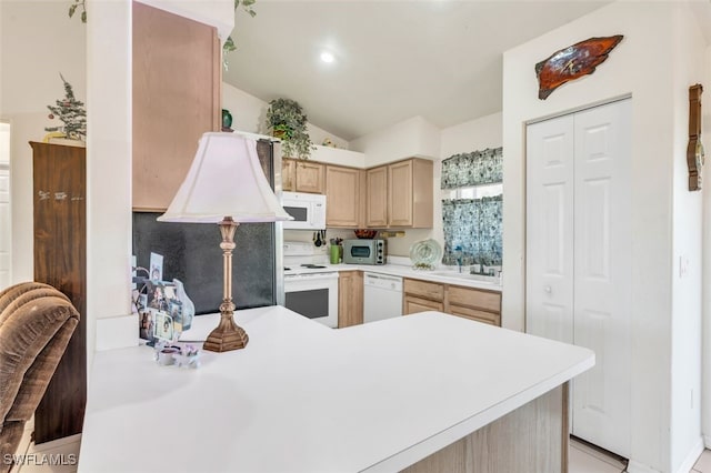 kitchen with white appliances, lofted ceiling, sink, light brown cabinetry, and kitchen peninsula