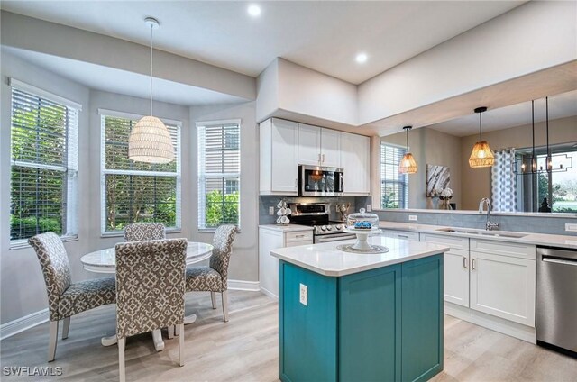 kitchen featuring a center island, sink, decorative light fixtures, white cabinetry, and stainless steel appliances