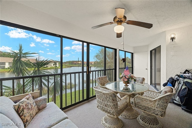 sunroom featuring ceiling fan and a water view