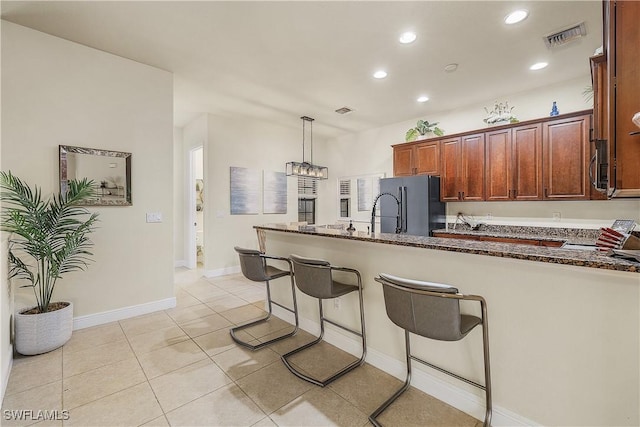 kitchen with dark stone countertops, light tile patterned floors, a breakfast bar, black fridge, and pendant lighting