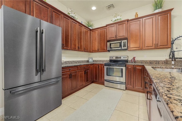 kitchen featuring stainless steel appliances, stone countertops, sink, and light tile patterned floors