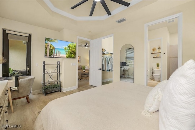 bedroom featuring ensuite bath, light hardwood / wood-style flooring, a spacious closet, a tray ceiling, and ceiling fan