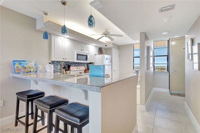 kitchen featuring white appliances, a kitchen breakfast bar, kitchen peninsula, hanging light fixtures, and white cabinetry