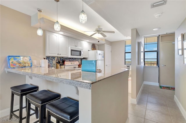 kitchen featuring white appliances, white cabinets, decorative light fixtures, kitchen peninsula, and a breakfast bar area