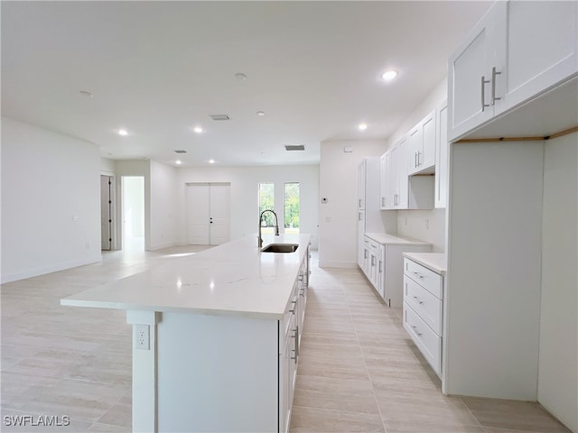 kitchen featuring light tile patterned flooring, a center island with sink, light stone countertops, sink, and white cabinets