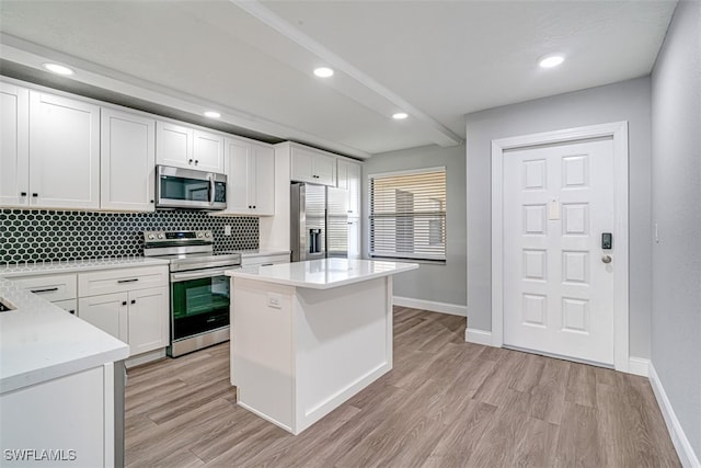 kitchen featuring tasteful backsplash, stainless steel appliances, a kitchen island, white cabinetry, and light hardwood / wood-style flooring