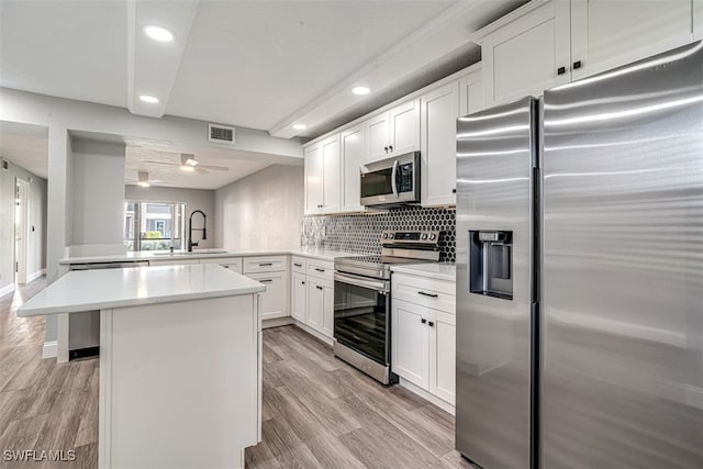 kitchen with stainless steel appliances, light hardwood / wood-style floors, white cabinets, kitchen peninsula, and sink