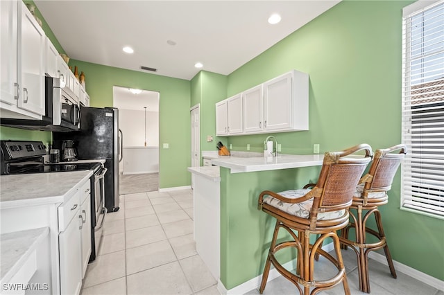 kitchen with light tile patterned flooring, kitchen peninsula, a kitchen breakfast bar, white cabinets, and electric range