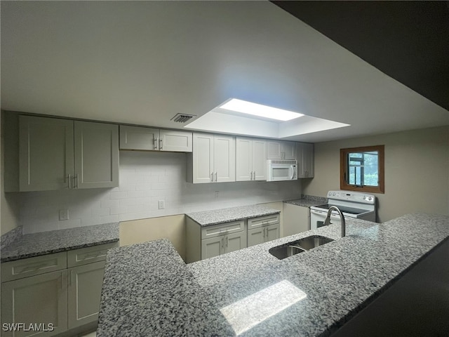 kitchen featuring tasteful backsplash, gray cabinetry, light stone counters, kitchen peninsula, and white appliances