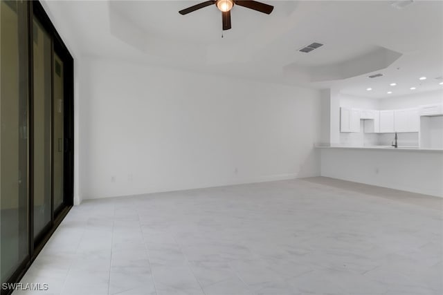 unfurnished living room featuring a raised ceiling and ceiling fan