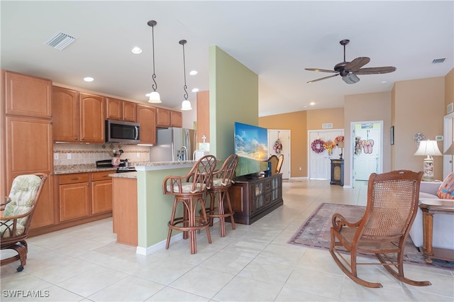 kitchen featuring appliances with stainless steel finishes, decorative light fixtures, tasteful backsplash, a kitchen breakfast bar, and light tile patterned floors