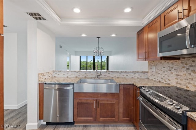 kitchen featuring sink, light wood-type flooring, appliances with stainless steel finishes, a tray ceiling, and backsplash