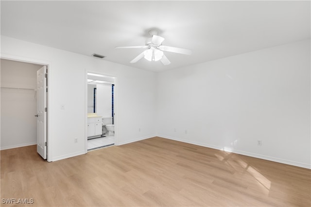 unfurnished bedroom featuring a closet, a walk in closet, ensuite bath, ceiling fan, and light hardwood / wood-style flooring