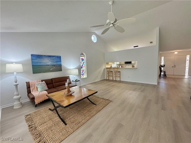 living room featuring light wood-style flooring, ceiling fan, high vaulted ceiling, and baseboards