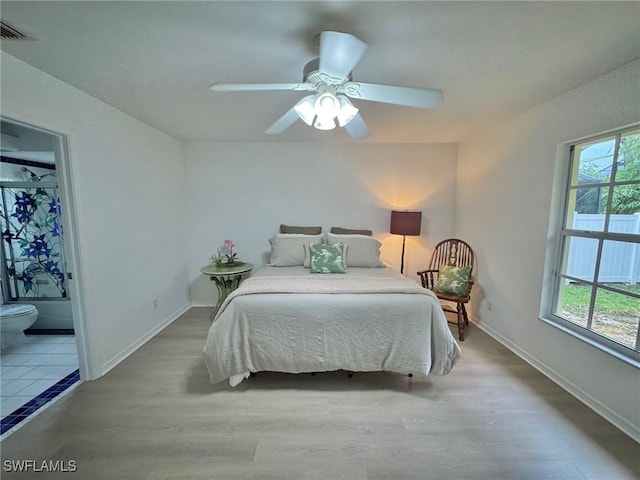 bedroom with wood finished floors, baseboards, ensuite bathroom, and a ceiling fan