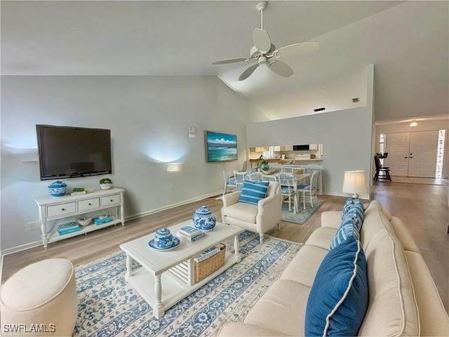 living room with lofted ceiling, ceiling fan, wood finished floors, and baseboards