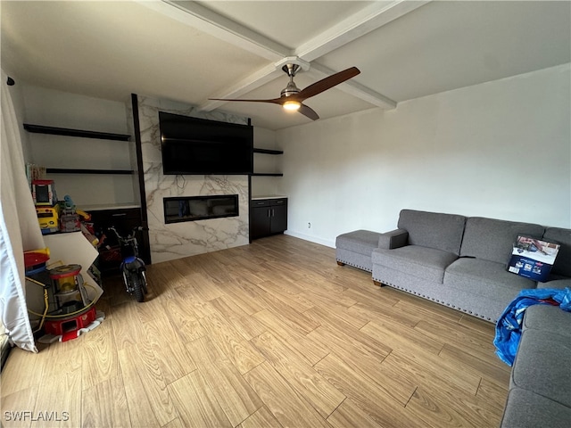 living room with ceiling fan, beamed ceiling, light wood-type flooring, and a high end fireplace