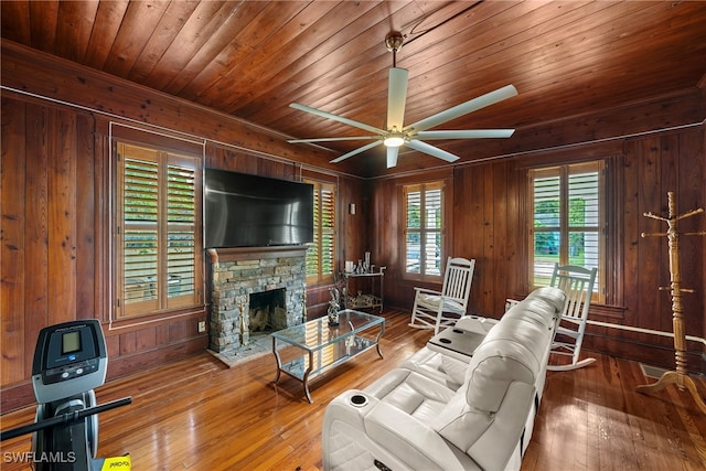 living room with a stone fireplace, wooden walls, hardwood / wood-style flooring, and ceiling fan