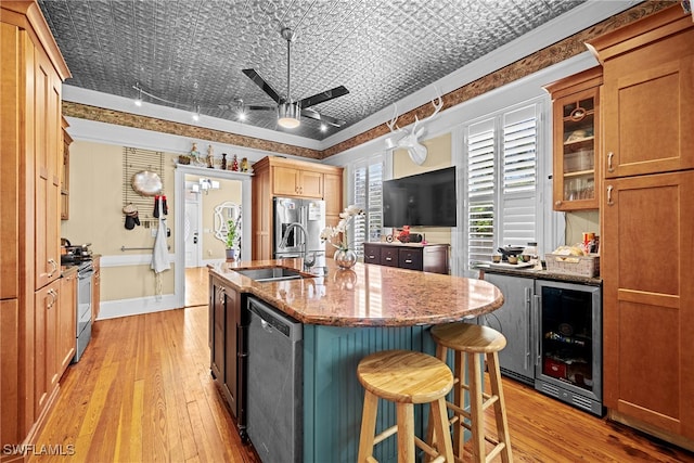 kitchen featuring beverage cooler, sink, a kitchen island with sink, light stone countertops, and appliances with stainless steel finishes