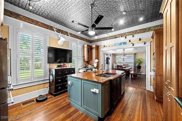 kitchen featuring stainless steel appliances, dark hardwood / wood-style flooring, dark stone counters, an island with sink, and ceiling fan