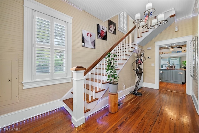 staircase featuring wood walls, a chandelier, and hardwood / wood-style floors