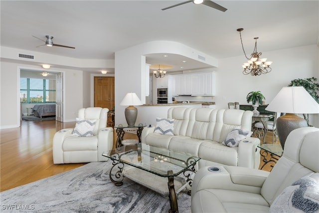 living room featuring ceiling fan with notable chandelier and light hardwood / wood-style flooring