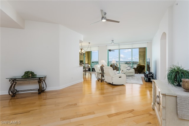 living room featuring ceiling fan with notable chandelier, light wood-type flooring, and a wall of windows