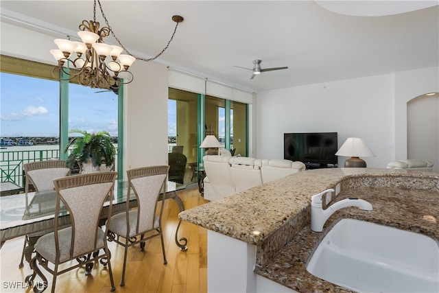 kitchen with a water view, sink, stone countertops, pendant lighting, and light hardwood / wood-style flooring