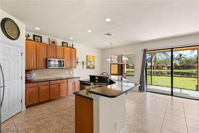 kitchen with backsplash, a kitchen island with sink, hanging light fixtures, sink, and appliances with stainless steel finishes