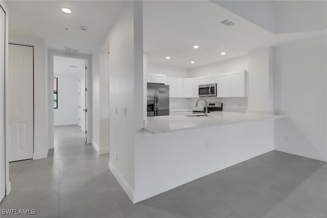 kitchen with sink, light tile patterned floors, kitchen peninsula, white cabinets, and appliances with stainless steel finishes