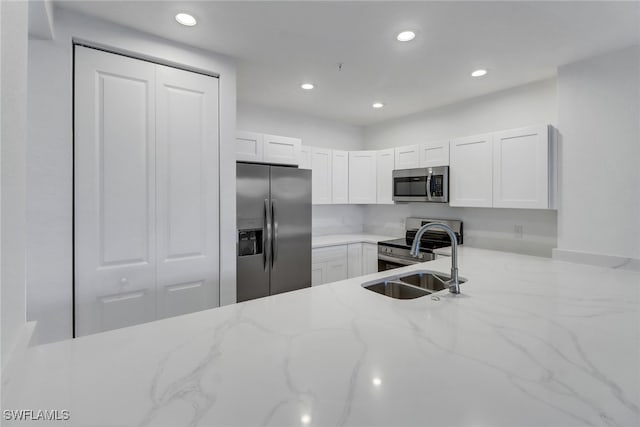 kitchen featuring appliances with stainless steel finishes, light stone counters, white cabinetry, and sink