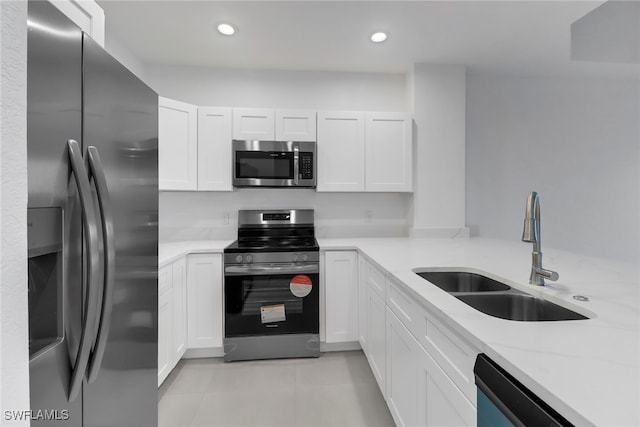 kitchen featuring light stone counters, stainless steel appliances, sink, light tile patterned floors, and white cabinetry